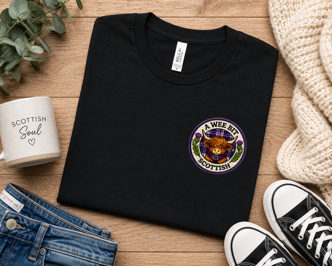 Folded A Wee Bit Scottish ladies t-shirt displayed with jeans, trainers and accessories in a Scottish-inspired flat lay scene.