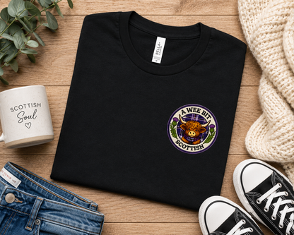 Folded A Wee Bit Scottish ladies t-shirt displayed with jeans, trainers and accessories in a Scottish-inspired flat lay scene.