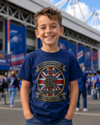 Young boy wearing the If You Cannae Dae The Bouncy youth t-shirt in navy, featuring the exact Union Flag crest design, standing outside a football stadium on match day.