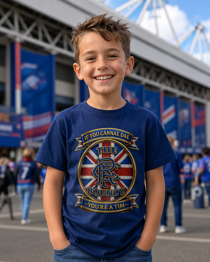 Young boy wearing the If You Cannae Dae The Bouncy youth t-shirt in navy, featuring the exact Union Flag crest design, standing outside a football stadium on match day.