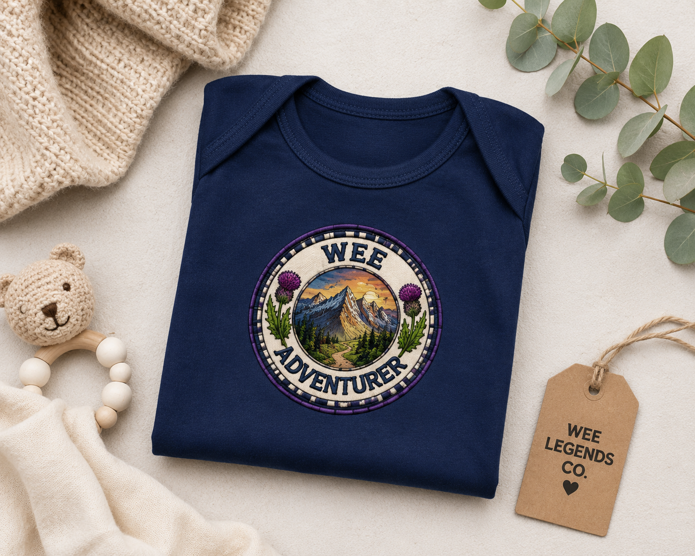 Folded navy Wee Adventurer baby bodysuit displayed with baby accessories and natural styling.