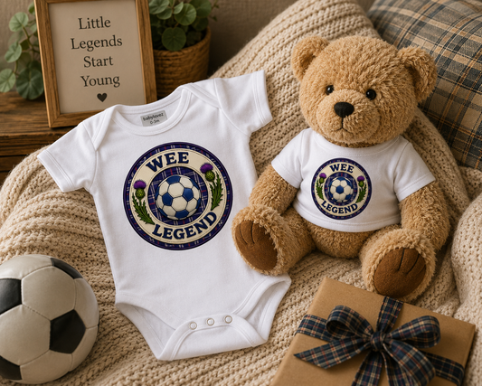 Wee Legend baby gift set featuring a matching bodysuit and teddy bear displayed on a cosy knitted blanket with football-inspired accessories.