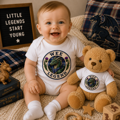 Smiling baby wearing the Wee Legend Dragon bodysuit alongside a matching teddy bear in a warm nursery setting.