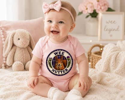 Happy baby wearing a pastel pink Wee Nutter baby bodysuit in a cosy nursery setting with soft toys.