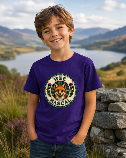Young boy wearing a purple Wee Rascal youth t-shirt featuring a fox badge design, standing on a countryside path with hills and loch views in the background.