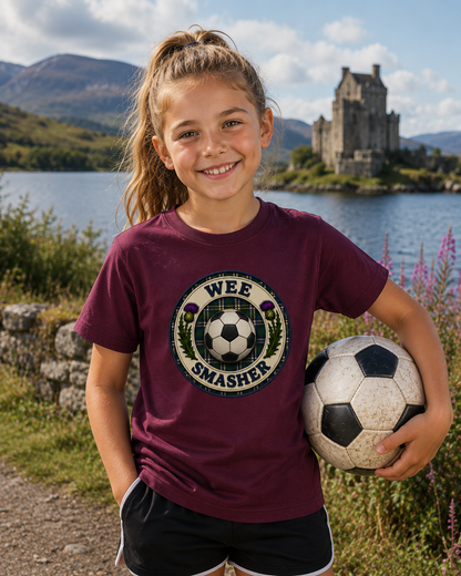 Young girl wearing a maroon Wee Smasher youth t-shirt featuring a football crest with centred football, standing beside a Scottish loch and castle.