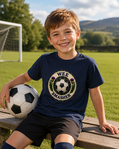 Smiling young football fan wearing a navy Wee Smasher youth t-shirt while sitting on a bench beside a football pitch with a football by his side.